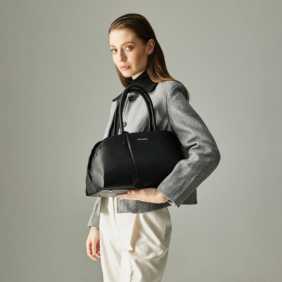Elegant woman styling a structured black Braun Büffel handbag with a grey jacket in a clean studio shoot